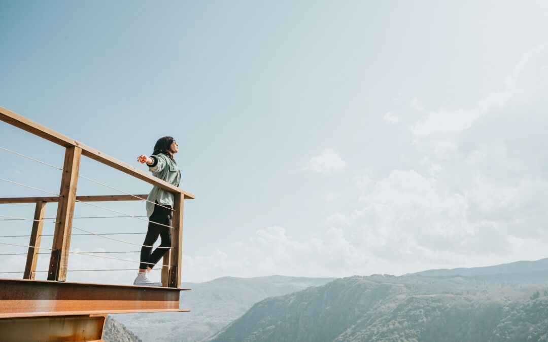 a woman with her arms spread wide enjoying freedom while standing on a balcony overlooking a scenic valley