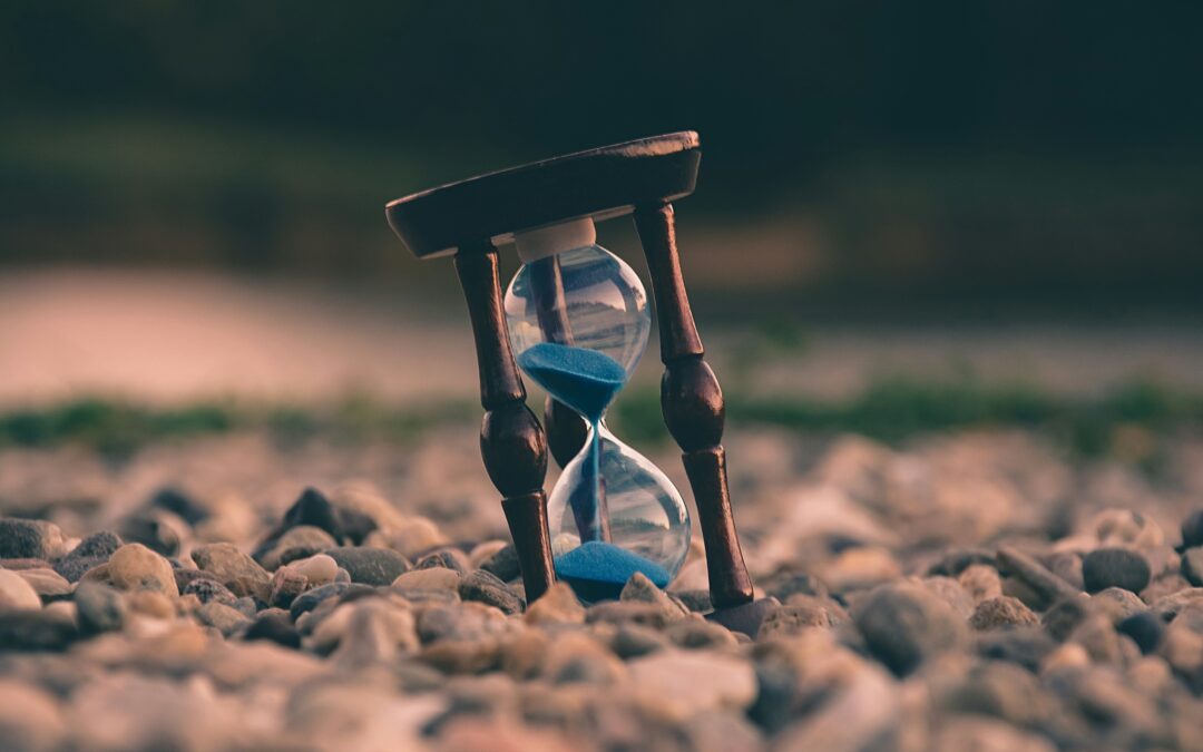 a wooden hour glass sits crooked on a bed of pebbles. Here's how to fix your time management tips.